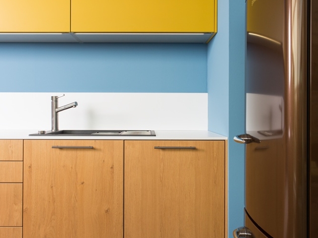 Küchenzeile mit Holzfront, gelben Hängeschränken und braunem, freistehenden Kühlschrank