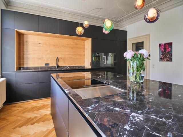 Küche mit Kochinsel und langer Küchenzeile mit grauen Fronten und marmorner Arbeitsplatte
