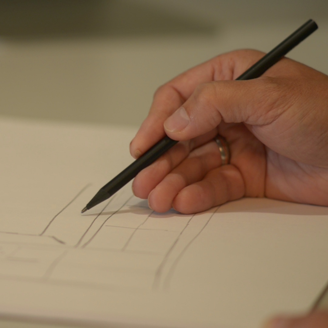 Männliche Hand, die mit einem schwarzen Bleistift eine Küchenplanung auf ein Papier skizziert