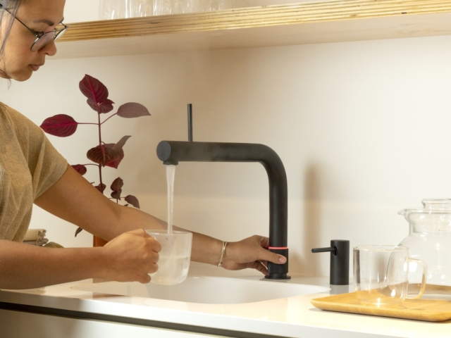 Frau gießt kaltes Wasser aus einem Quooker Wasserhahn in ein Glas