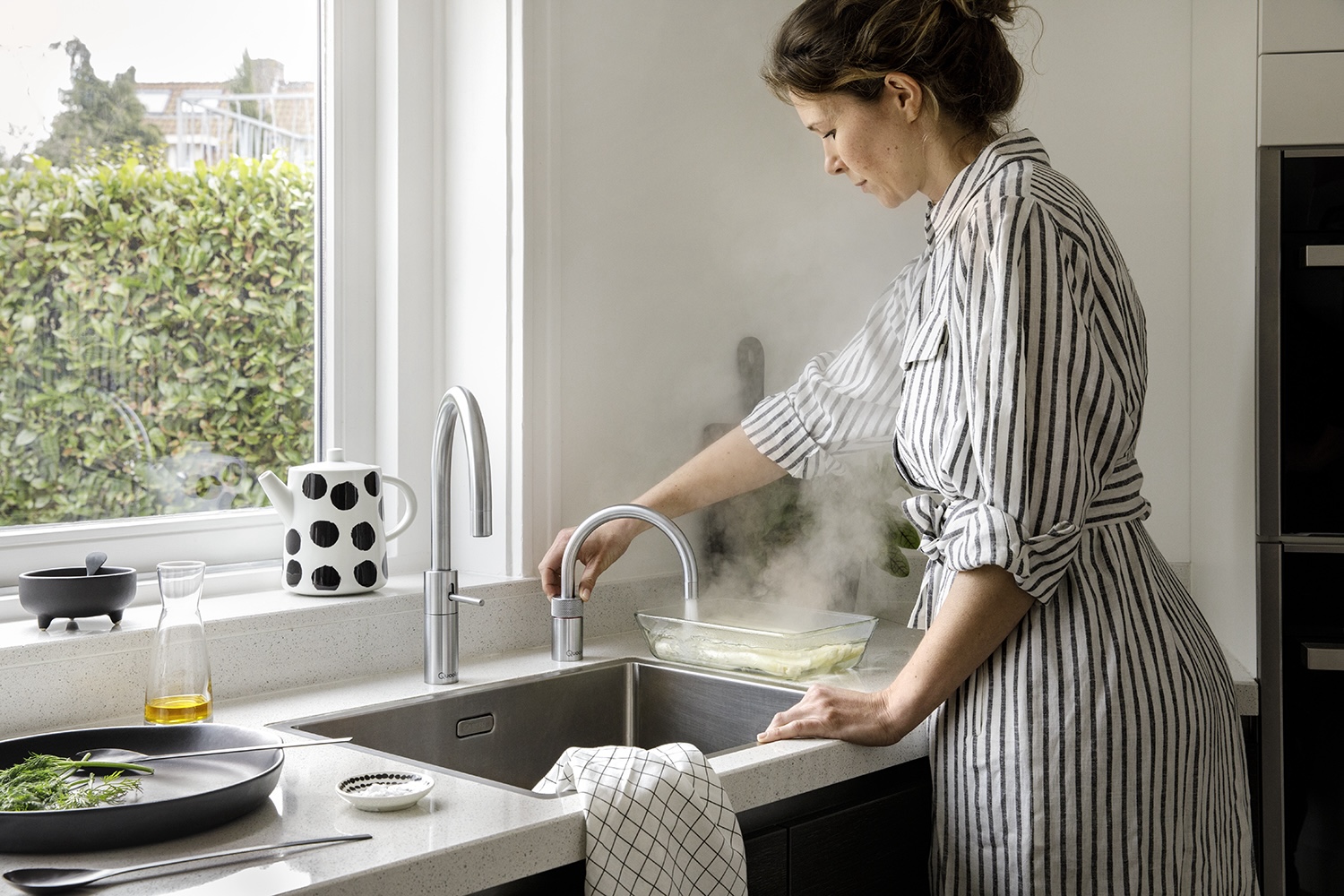 Frau lässt kochendes Wasser in eine Glasschale aus dem Quooker Wasserhahn fließen